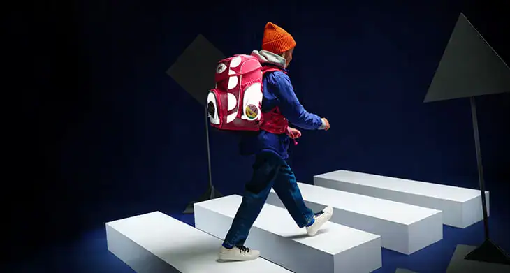 Ein Kind läuft mit einem reflektierenden Schulranzen von ergobag durch eine imaginäre Verkehrsszene.