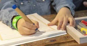 Nahaufnahme einer Kinderhand, die mit einem Schulfüller von LAMY in ein Schulheft schreibt