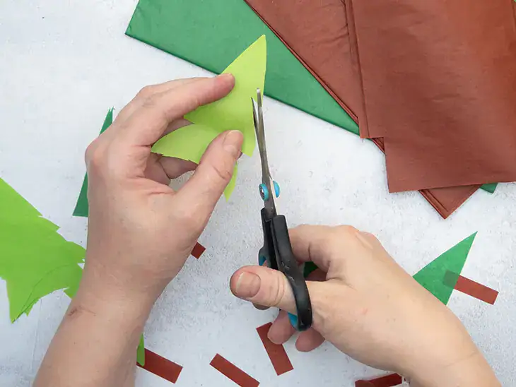 Jemand schneidet aus Seidenpapier von HEYDA Tannenbäume aus. Foto: Johanna Rundel