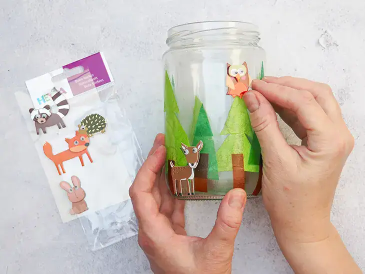 Jemand klebt kleine Waldtieraufkleber von HEYDA auf ein selbstgebasteltes Windlicht. Foto: Johanna Rundel