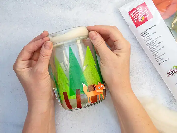 Jemand bestreicht Bäume aus Seidenpapier von HEYDA mit Kleber auf ein Glas. Foto: Johanna Rundel