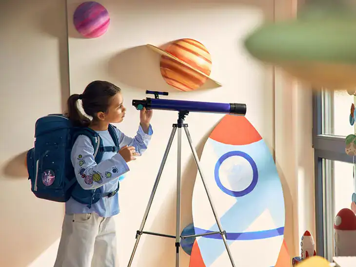 Ein Kind steht mit Schulranzen von ergobag vor einem Teleskop.