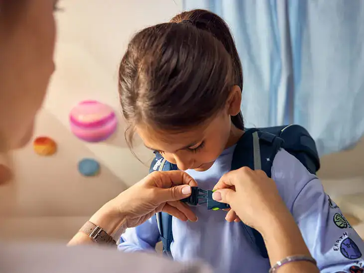 Eine Mutter stellt den Schulranzen ihrer Tochter ein.